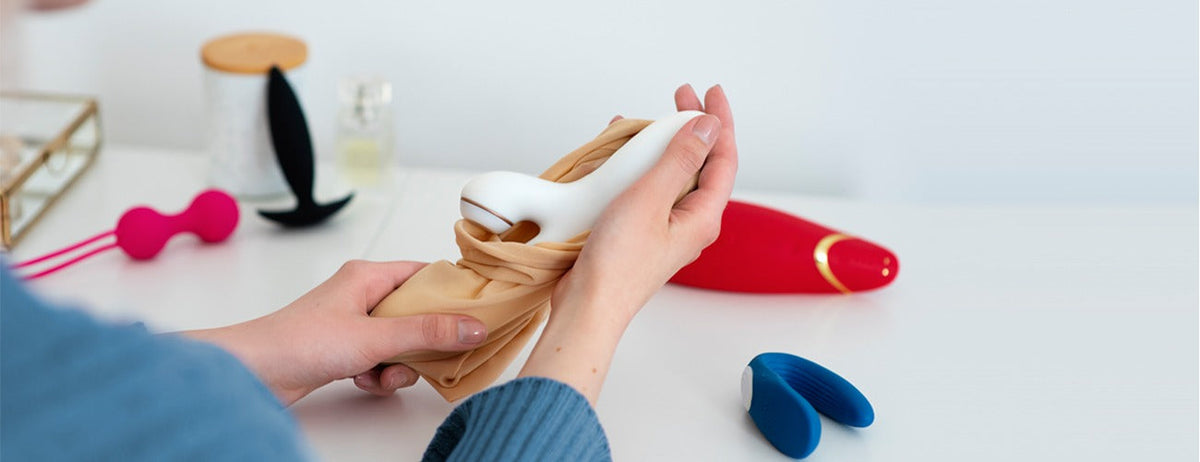 White curved vibrator in body-safe silicone, held with beige fabric, rechargeable design.