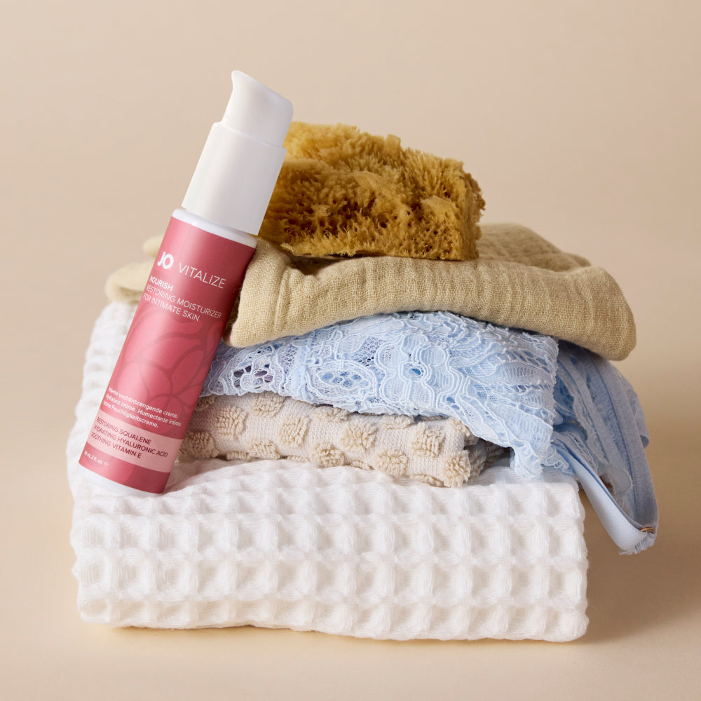 Vitalize Nourish bottle beside folded towels, lace lingerie and a gold lipstick