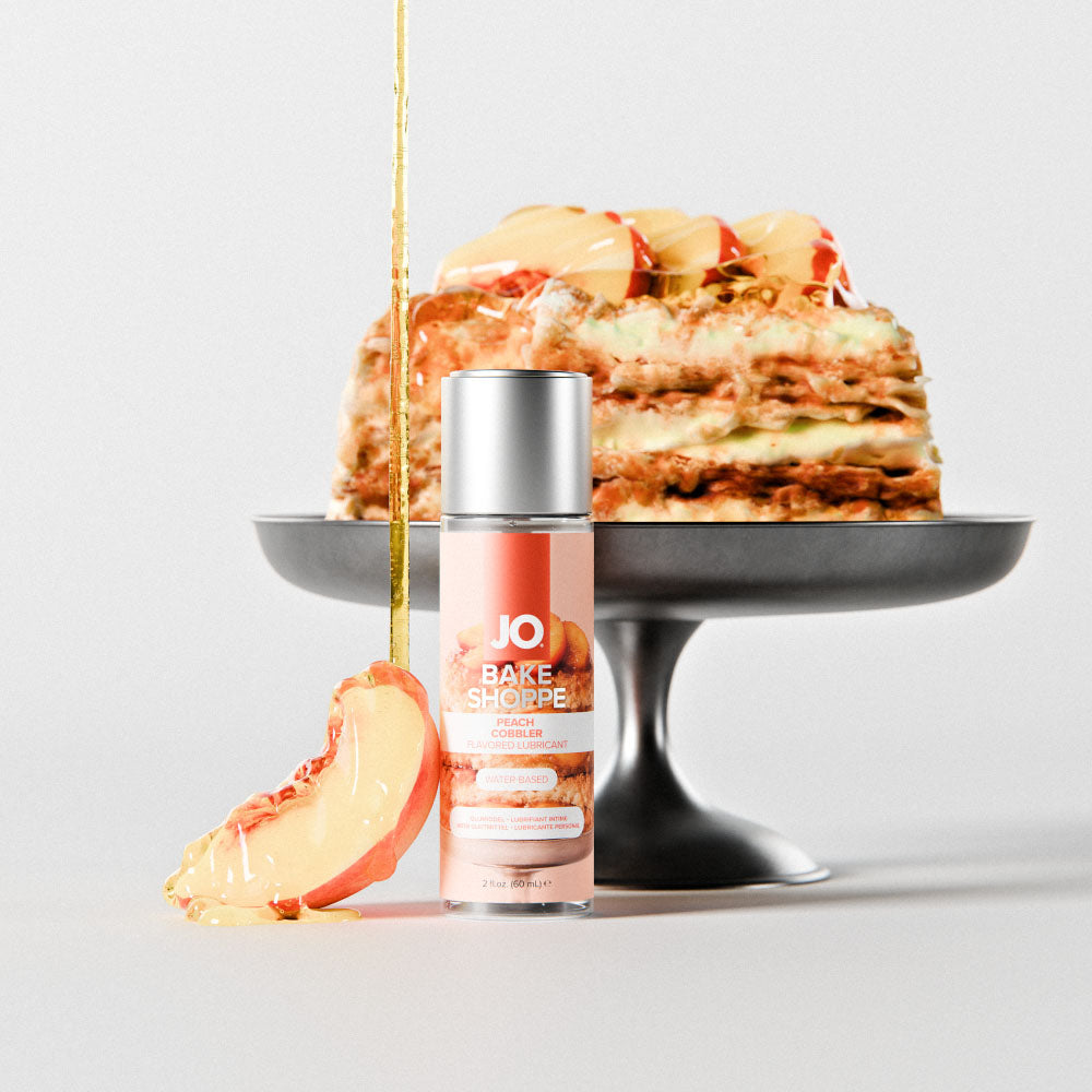 Peach Cobbler bottle on a cake stand beside a peach dessert drizzled with syrup