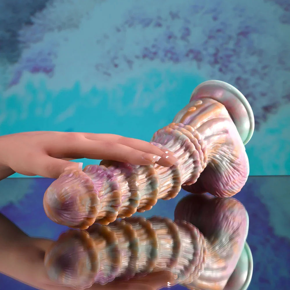 Evolved Fantasy dildo in multicolour lying flat with a hand resting on the ridged shaft