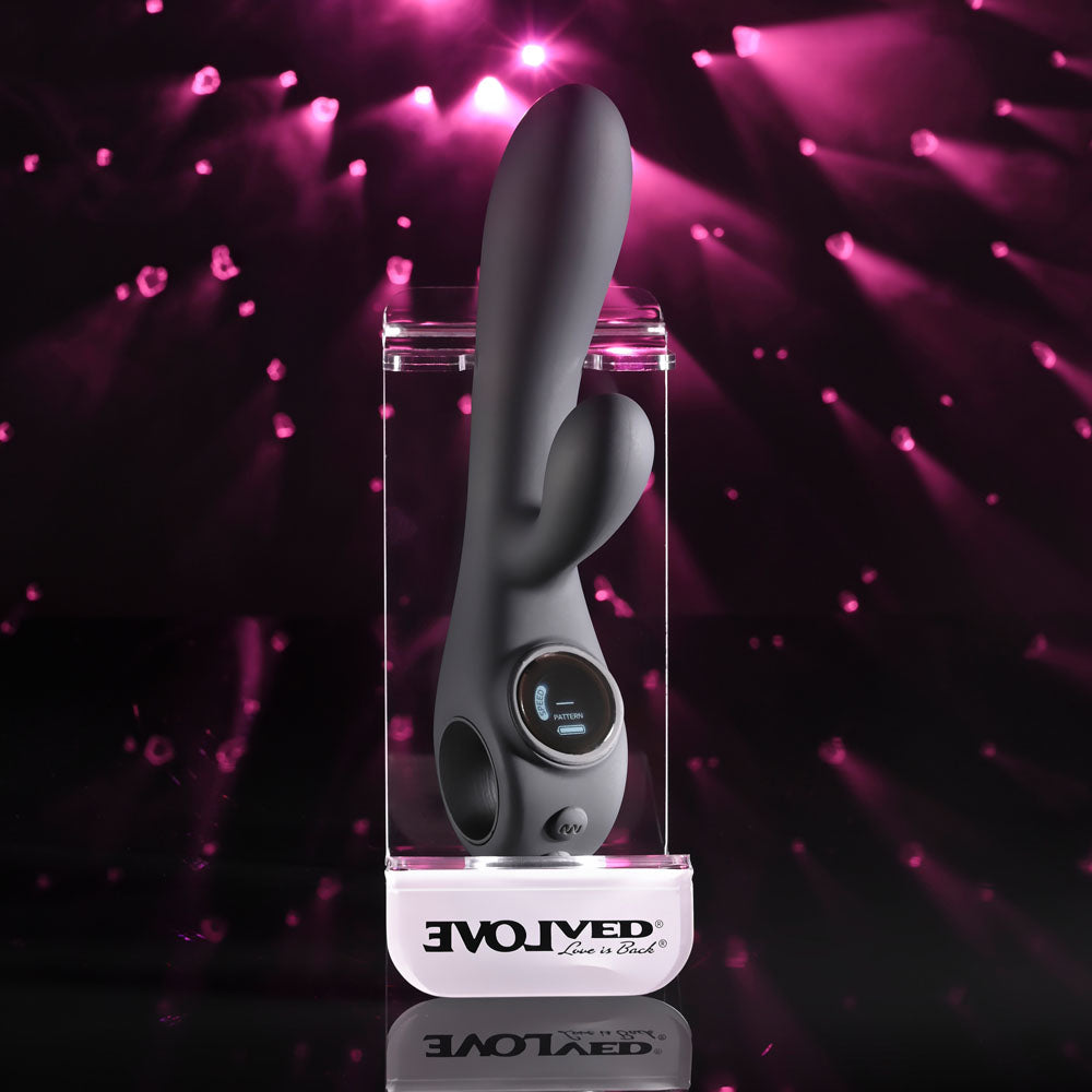 Evolved Black Magic in Black upright on a clear Evolved display stand, pink lights behind