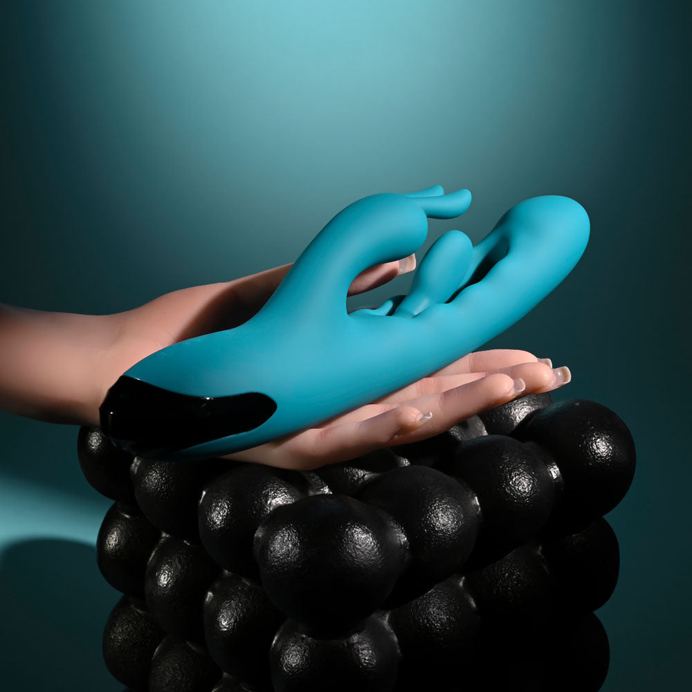 Evolved Bunny Tapper in Teal lying across an open hand above a stack of black spheres
