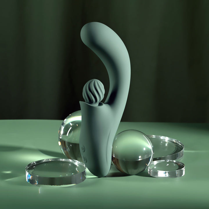 Evolved Spiral Charm in sage green standing among clear glass spheres and discs, green backdrop