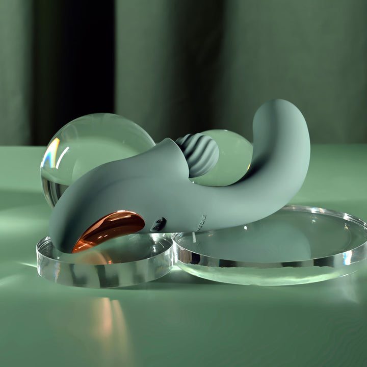 Evolved Spiral Charm in sage green lying flat at an angle, glass sphere behind it