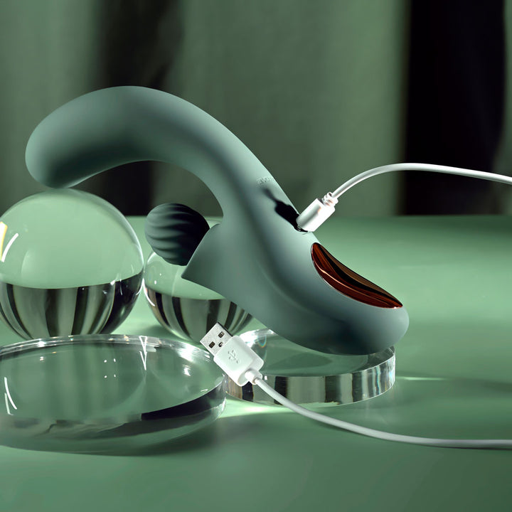 Evolved Spiral Charm in sage green lying flat with its white USB charging cable attached