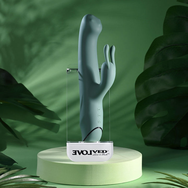 Evolved Satin Swirl in sage green upright on a clear Evolved stand, monstera leaves behind