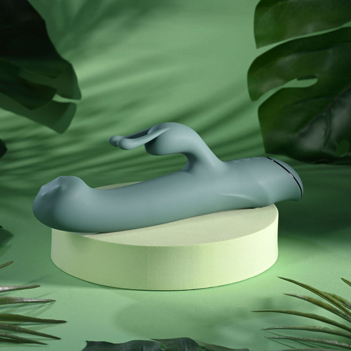Evolved Satin Swirl in sage green lying on a pale podium, rabbit ears up and tip to the left