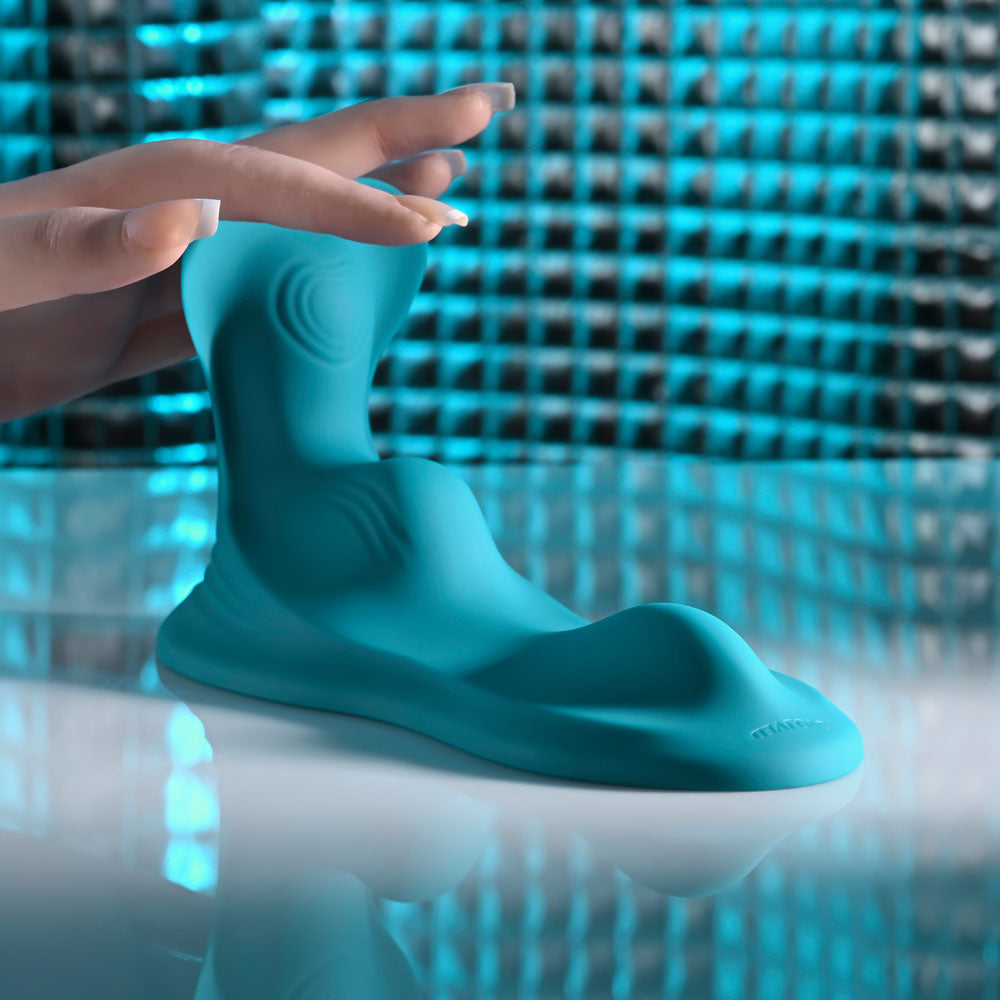 Evolved Bump & Grind stimulator in Teal on a reflective surface, a hand reaching in above it