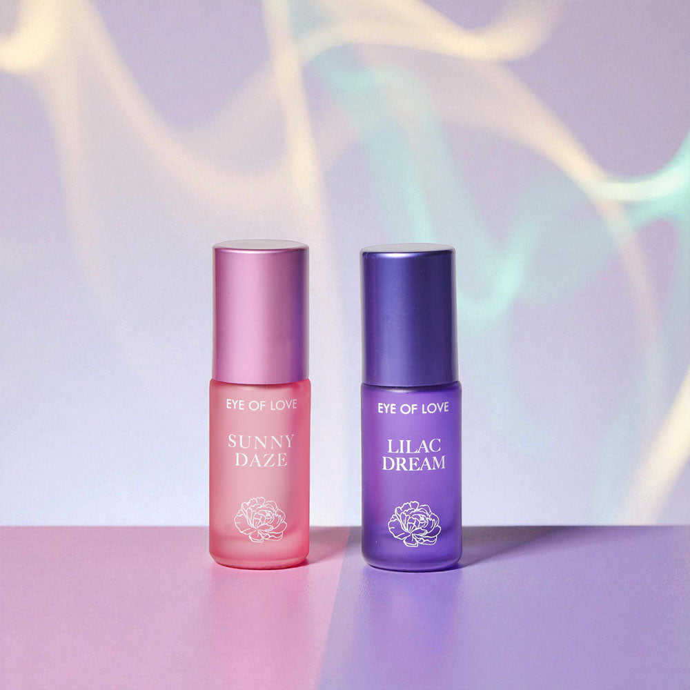 Pink Sunny Daze and purple Lilac Dream roll-on bottles on an iridescent backdrop