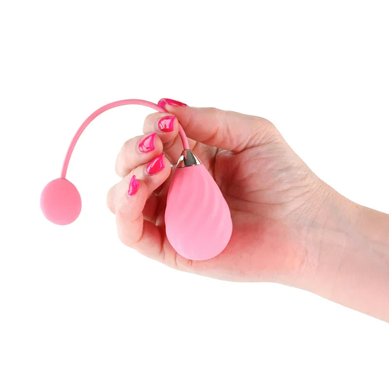 Techno Kandi vibrating egg in Pink held in a hand by its cord, remote fob hanging