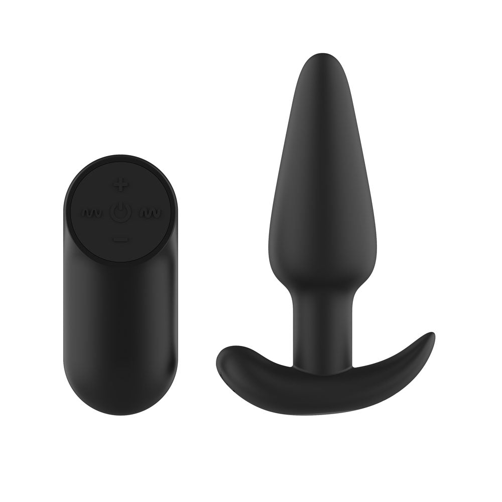 Passion Play Silicone Vibrating Butt Plug in Black beside its oval remote, curved base
