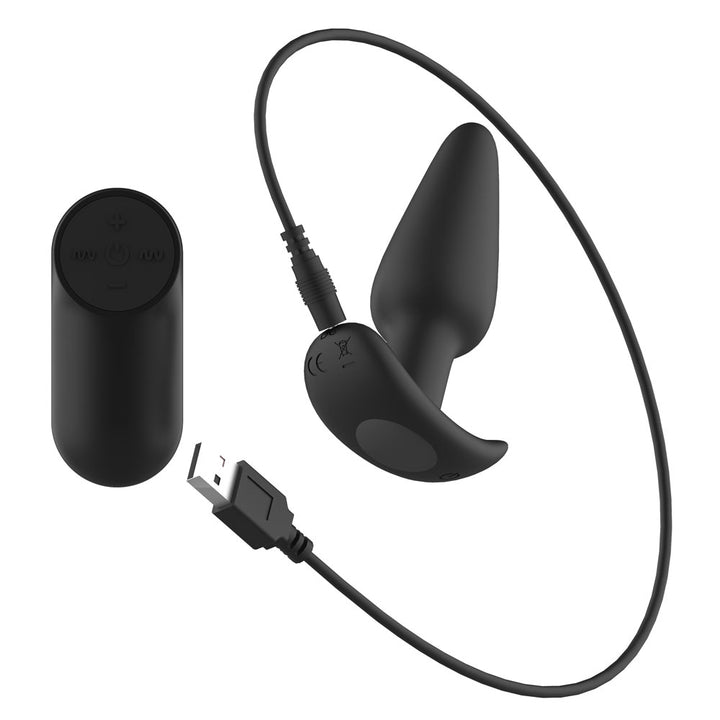 Passion Play Vibrating Butt Plug in Black with its USB charging cable plugged in, remote at left