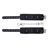 EDGE Handcuffs - Black Restraints boast black leather wrist cuffs with precise stitching and silver buckles. A detachable metal chain fastens to small loops, providing secure restraint. Adjustable buckles ensure a perfect fit, all showcased elegantly against a white background.