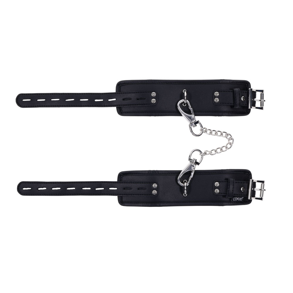 The EDGE Handcuffs - Black Restraints have black leather with an adjustable buckle, secure constraint design, padded interiors for comfort, and metal rivets for durability. A short silver chain with carabiners connects the cuffs.