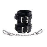 The EDGE Handcuffs - Black Restraints are crafted from smooth black leather, featuring an adjustable buckle closure and a durable silver chain for secure restraint. They showcase intricate craftsmanship with visible stitching and multiple size adjustment holes.