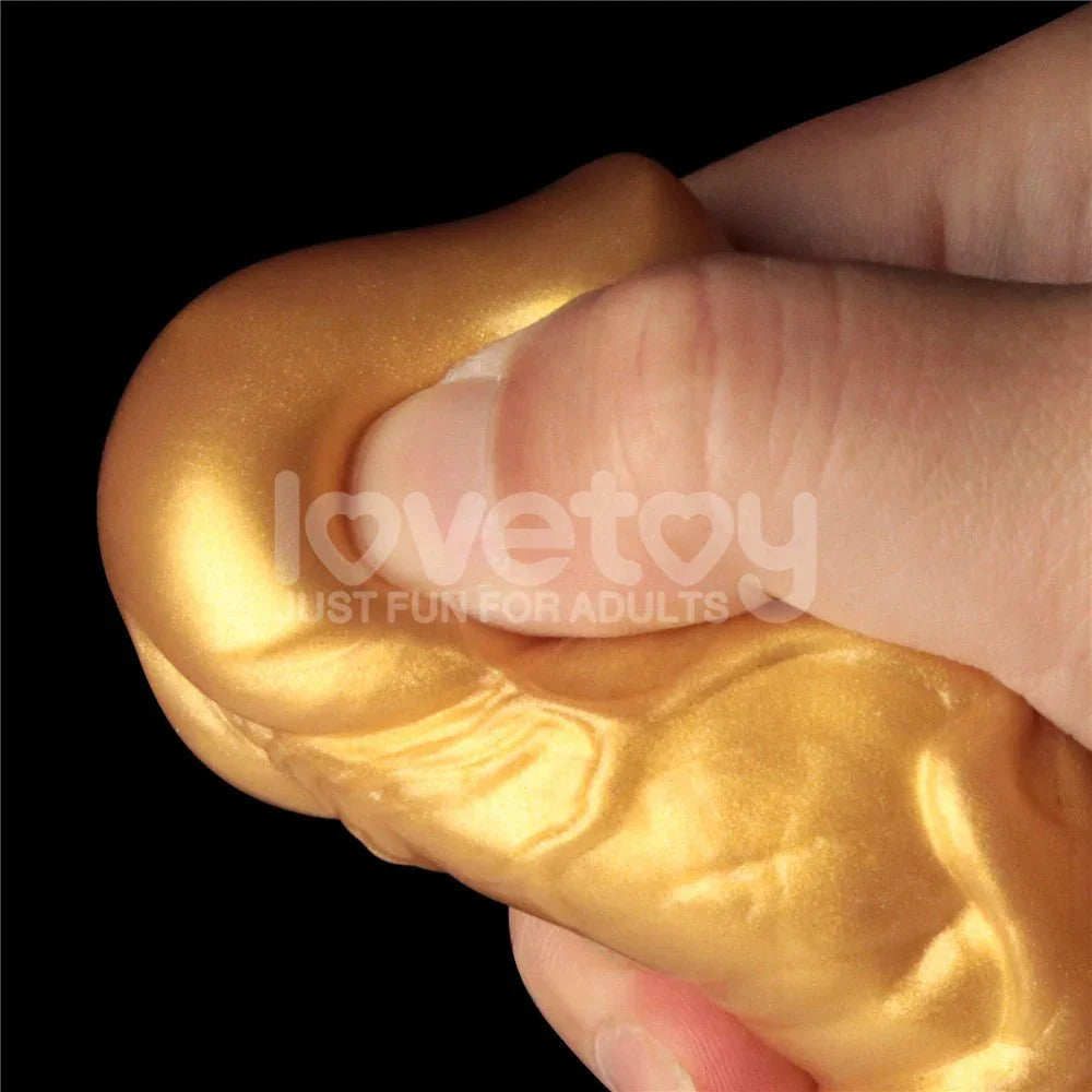 Fingers pinching the gold shaft of the Aerosx 7.5 inch dildo to show the soft outer silicone