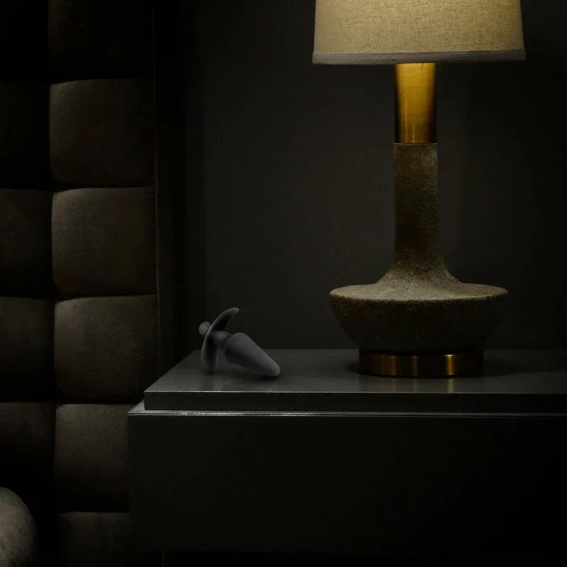 Black Anal Adventures vibrating plug resting on a dark bedside table beside a lit lamp