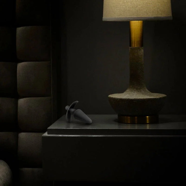 Black Anal Adventures vibrating plug resting on a dark bedside table beside a lit lamp