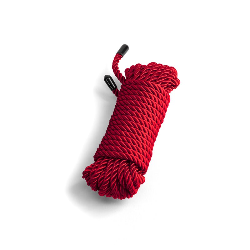 A neatly coiled bundle of Bound Rope - Red Bondage Rope, made from durable polyester fiber with two black plastic tips, lies on a plain white background. The shadow on the left indicates a light source from the right, revealing its thick and sturdy texture over a 7.6-meter length.