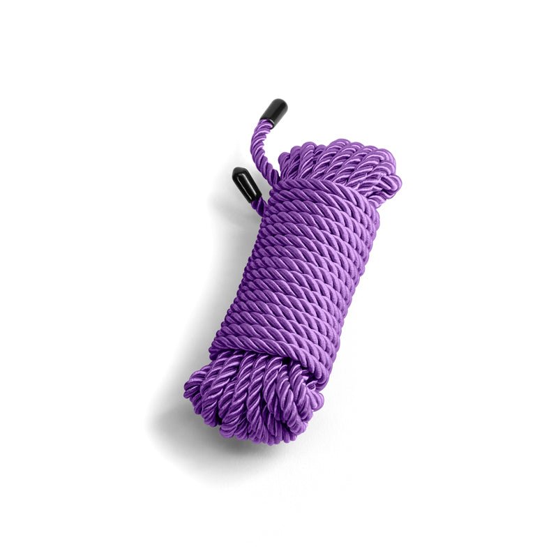 A neatly coiled Bound Rope - Purple sits on a white background, crafted from polyester for its non-chaffing property. The twisted design forms a spiral pattern with its glossy texture and black plastic end caps shining under overhead lighting, casting soft shadows to one side.