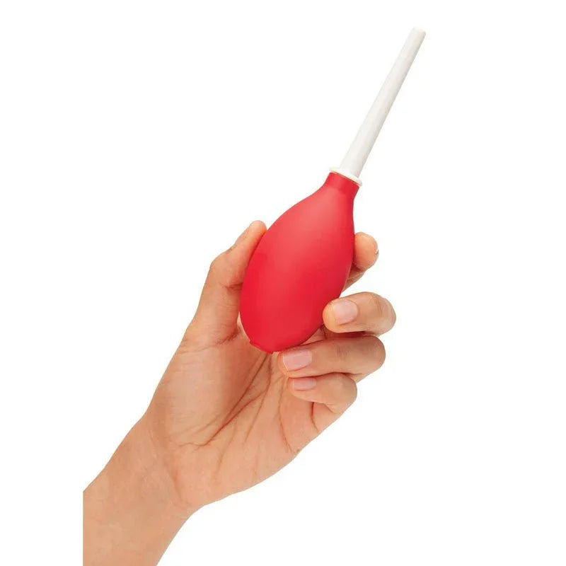 A hand squeezing the red CleanScene mini travel douche bulb, white nozzle upright