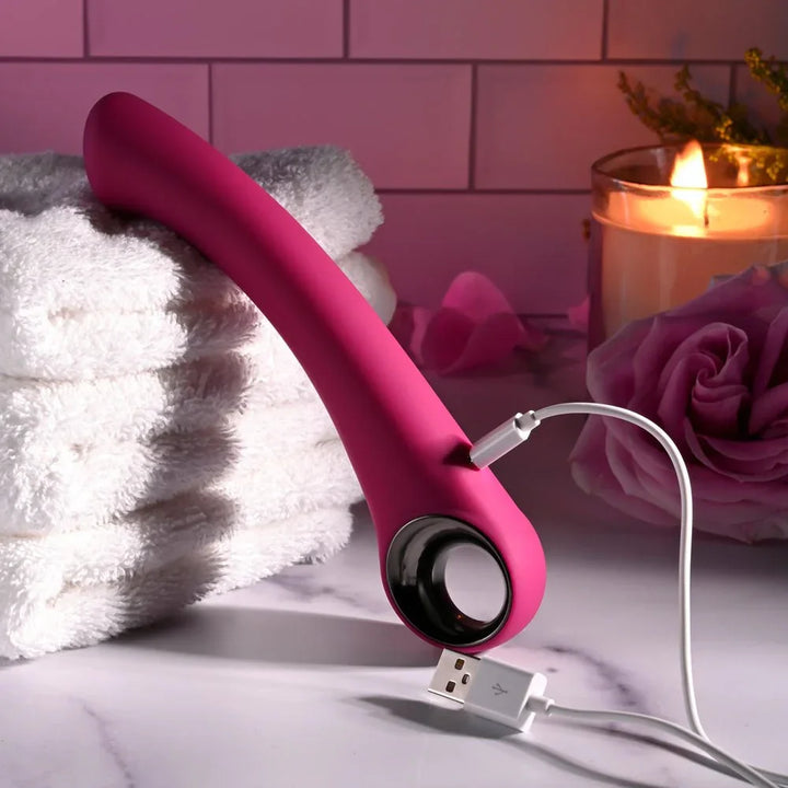 Evolved Pleasure Curve in Pink propped on folded towels with its USB charging cable attached