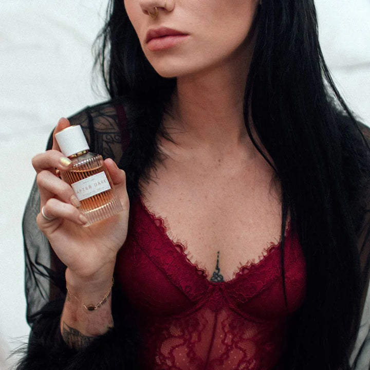 Model in a red lace bodysuit holding the Eye Of Love After Dark perfume bottle