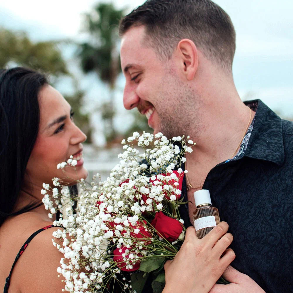 Smiling couple with a bouquet, After Dark perfume bottle held against his shirt