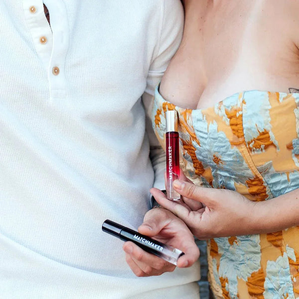 Couple standing close, each holding one Matchmaker Couples Kit vial, red and black