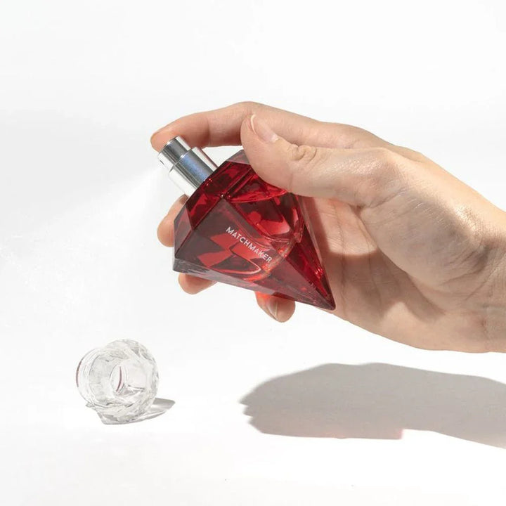 Hand holding the Matchmaker Red Diamond bottle, crystal stopper resting on white