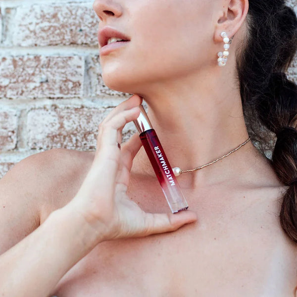Woman applying the Matchmaker Red Diamond 10ml vial to her neck against a brick wall