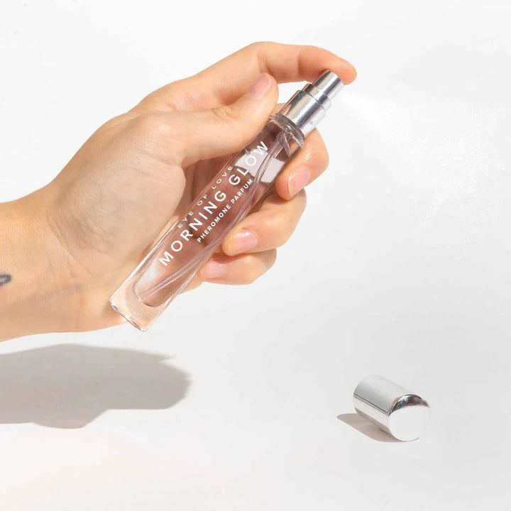 A hand spraying the Morning Glow 10ml vial, silver cap lying on the surface