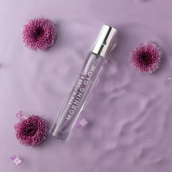 Morning Glow 10ml vial lying in lilac water with purple chrysanthemum blooms
