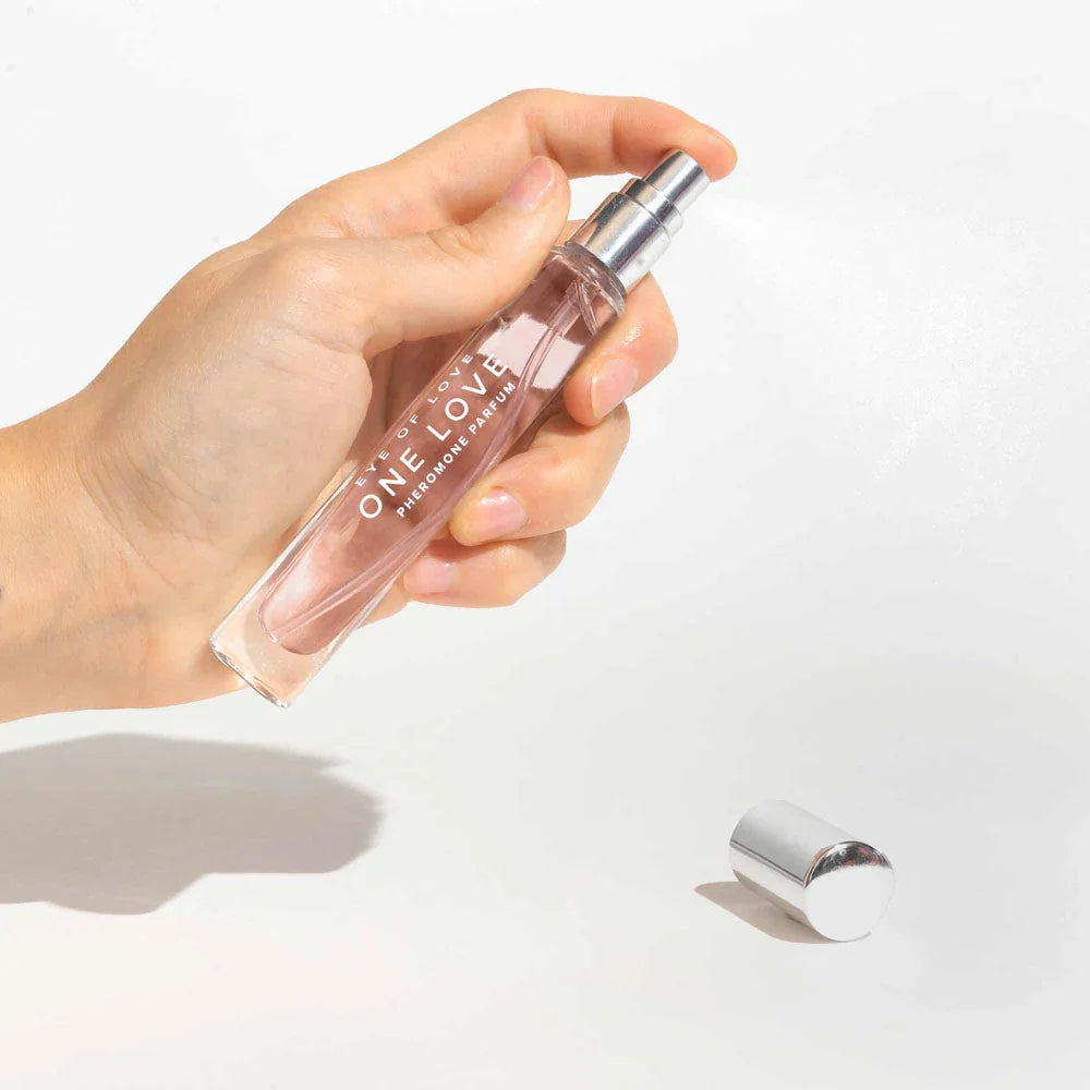 A hand spraying the One Love 10ml vial, silver cap lying on the surface
