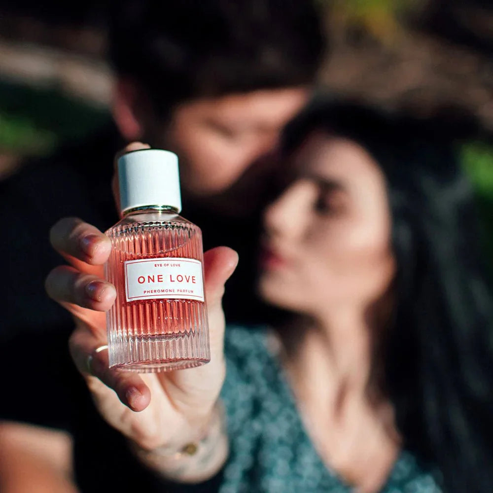 Hand holding the Eye Of Love One Love bottle to camera, a couple blurred behind