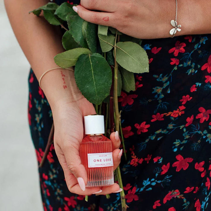 Woman in a floral dress holding the One Love bottle and a long-stemmed rose