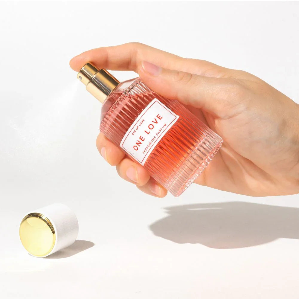 A hand spraying the Eye Of Love One Love 50ml bottle, gold cap lying on the surface