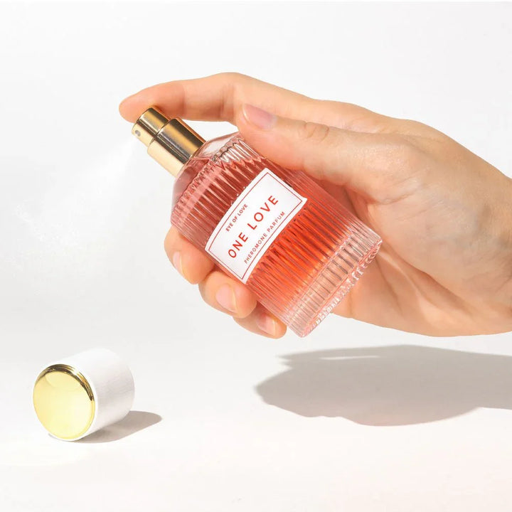 A hand spraying the Eye Of Love One Love 50ml bottle, gold cap lying on the surface