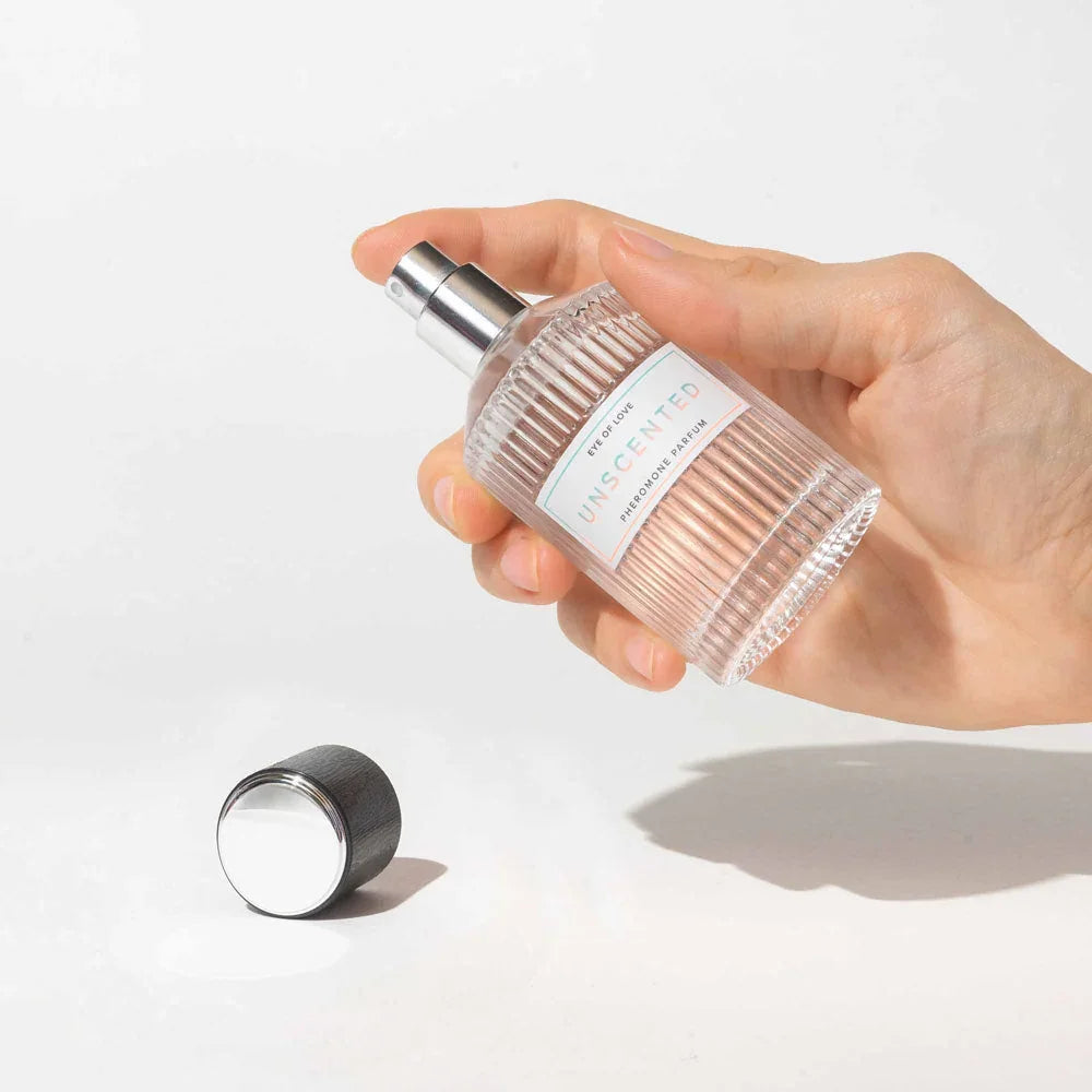 A hand holding the Eye Of Love Unscented Pheromone Perfume 50ml bottle, silver cap alongside