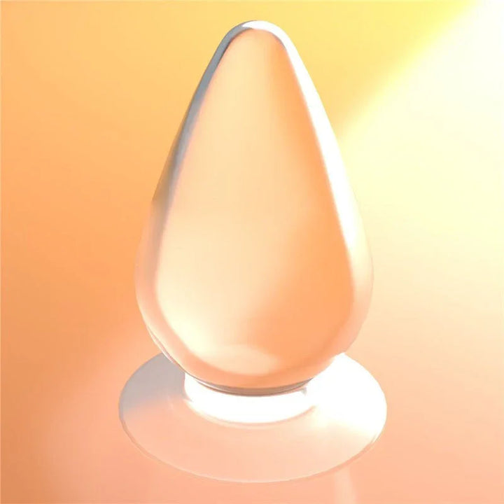 Flawless Clear anal plug lit against a warm orange backdrop, showing the smooth teardrop shape