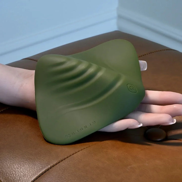 Gender X Pleasure Pad in Green lifted by a hand from the leather ottoman
