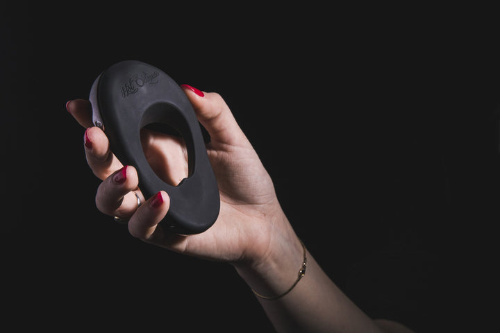Hand holding the black Hot Octopuss Atom Plus ring against a dark backdrop