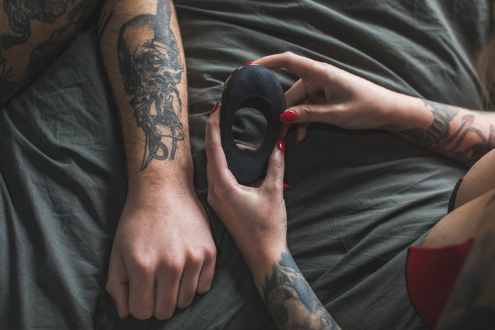 Woman holding the Atom Plus beside her partner on grey bed sheets
