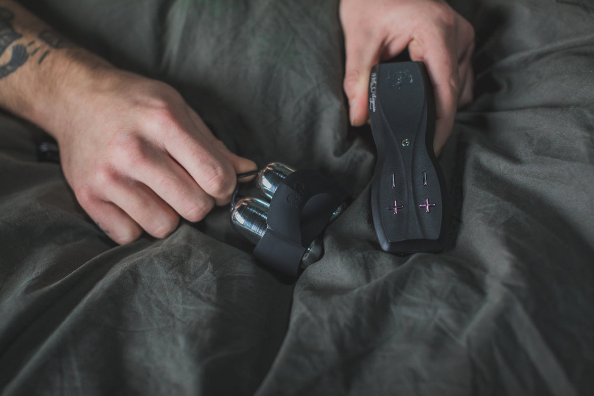 Hands holding the Jett's twin silver bullets and its black remote on grey sheets