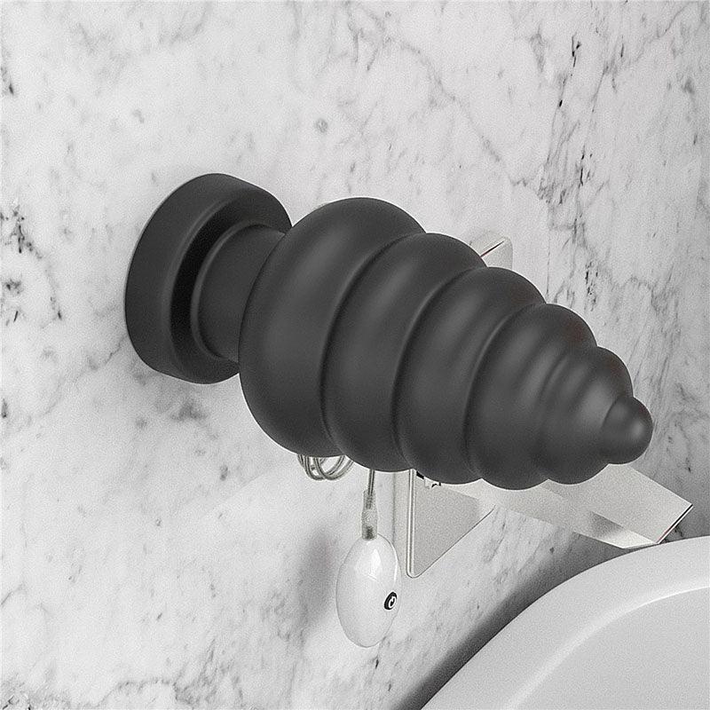 Black Anal Cracker suction-mounted on a marble bathroom wall with the remote hanging