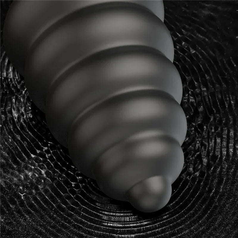 Black Anal Cracker plug photographed on a dark textured surface, ribs catching the light
