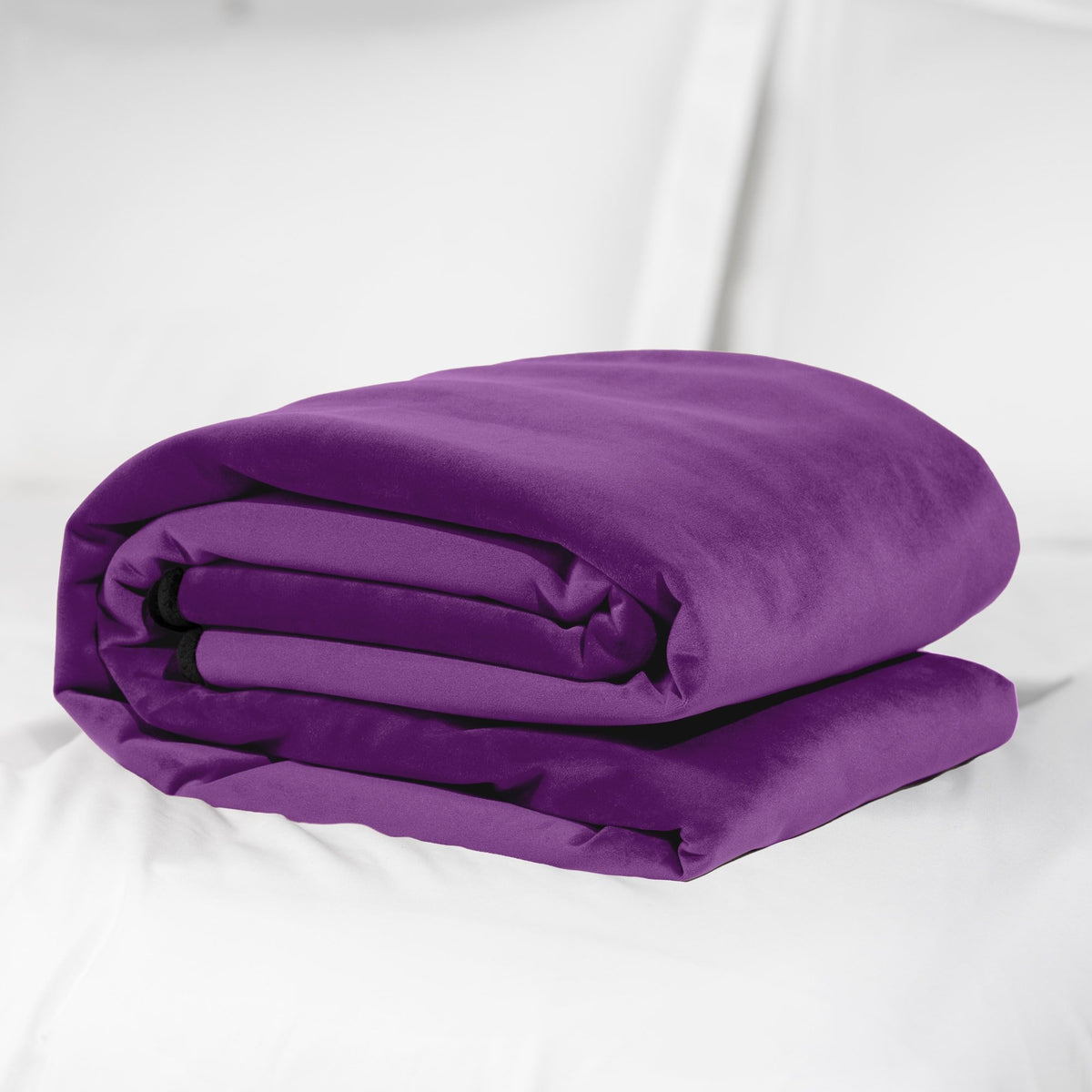 Purple Fascinator throw folded into a neat stack on a white bed