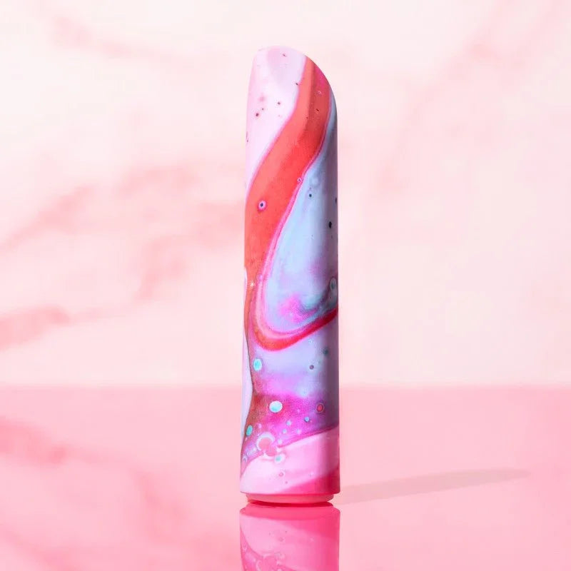 Fascinate bullet standing upright against a pink marble backdrop, pink and blue swirls