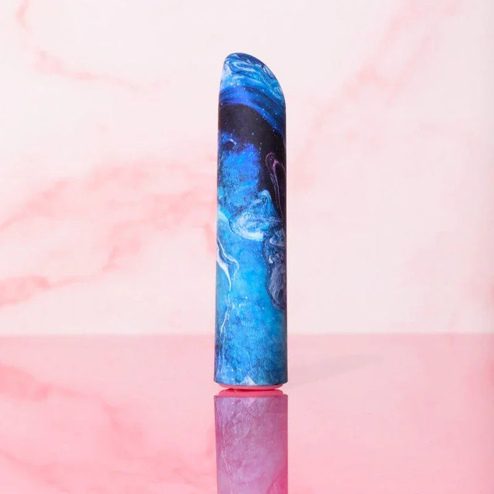 Blue Mesmerize bullet standing upright against a pink marble backdrop