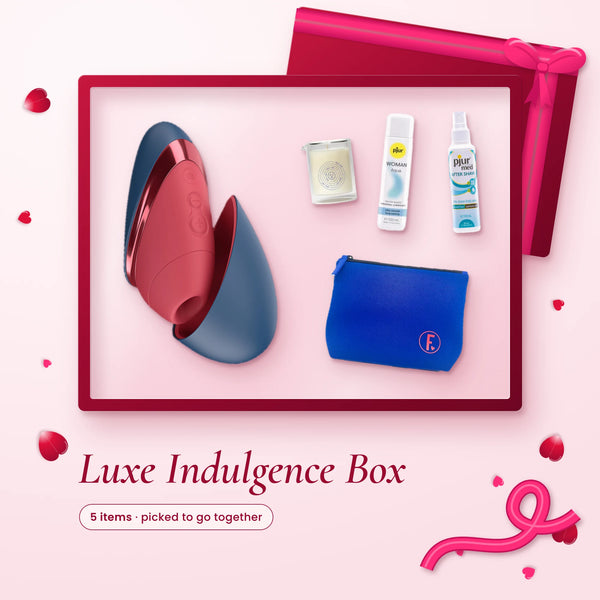 Luxe Indulgence Box: a Womanizer Next Liberty, Dame massage candle, pjur lube, pjur spray and a blue toy bag on pink
